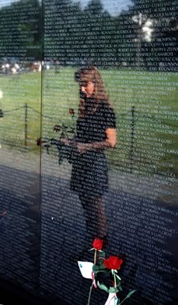 A young woman dressed in black is reflected on the polished surface of the memorial