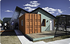 Photo of a small modular house featuring solar panels on its steeply-sloped roof.