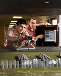 Using model farm buildings, silos, and trees (wire mesh coils serve as trees), agronomist (left) and soil scientist evaluate the effect of model arrangements on airflow: Click here for full photo caption.