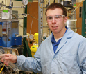 Photo of Edward Kunkes in the lab next to a reactor system used to convert sugar to gasoline.