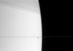 The small, dark form of Janus cruises along in front of bright Saturn. The 
edge-on rings cast dramatic shadows onto the northern hemisphere
