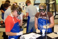 students in a laboratory working on experiments with their goggles on and taking notes 
