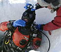 Photo shows a man helping another man prepare to leave the dive hole.