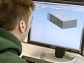 A male college student works at a computer with a 3-D image of a rectangular object on the screen.