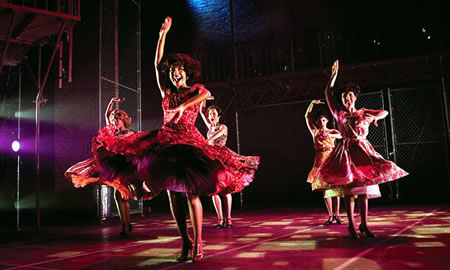 Five dancers in red dresses facing front having just finished a twirl		