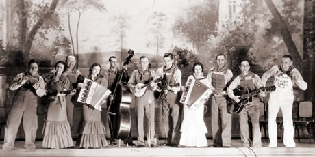     Archival black and white photo of eleven member of a country band onstage in front of a painted country scene  						