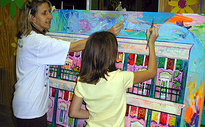 A woman and a girl  paint a colorful design on a board		
