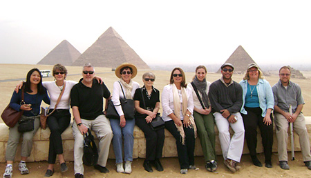         Ten men and women sitting in a row with Egyptian pyramids behind them  										