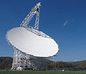 Telescope's broad white dish aims upward at a nearly cloudless sky.