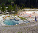 Photo of a woman standing near a hot spring with trees in background