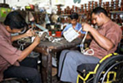 A factory worker using a wheelchair works along side co-workers who do not have disabilities.