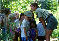 [Photo]: Forest Service ranger leaning over and 
talking to a group of children.