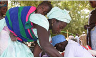 At a fair in Touba Toul, a Senegalese merchant with her infant strapped to her back exchanges her produce for USAID-funded seed vouchers - Click to read this story