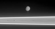 Lit by reflected light from Saturn, Enceladus appears to hover above the gleaming rings, its well-defined ice particle jets spraying a continuous hail of tiny ice grains