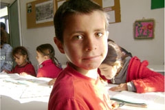 A young boy in a classroom looks into the camera