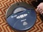 woman seated on rug next to blue, circular device labeled Roomba