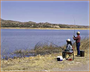 two people fishing on edge of lake