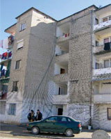 Photo of a worn five-story apartment building made of beige brick and concrete.