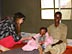 Photo of Dr. Peterson sitting with a father and child at a theraputic feeding center.