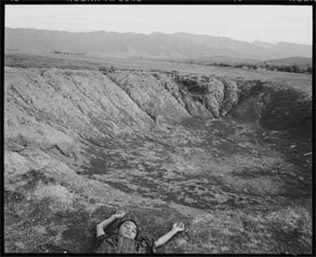 Photo: A young boy lies next to a crater made by a bomb.
