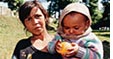 Photo of a woman holding a young infant, who has an orange in its hands.
