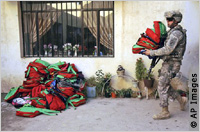 Soldier carrying backpacks, pile of backpacks on ground (AP Images)