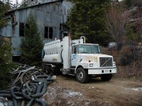 photo - "GapVax" truck backed up to dilapidated tin building. hoses and debris beside truck.