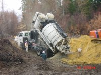 photo -  workers with respirators observe and water down rocks and sand being dumped on yellow pile.