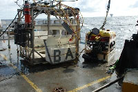 On the deck before deployment, the SeaEYE Falcon ROV on right sitting next to garage on left are prepped and ready for launch. The ROV garage is equipped with bioboxes (A,B), tube cores on far left, USBL Responder, CTD, and tether system (red and yellow cables). The ROV contains a number of instruments, including video and still cameras, LED array and halogen lights, and manipulator arm. - (photo credit: USGS DISCOVRE Expedition) - click to enlarge