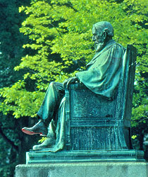 Bronze statue of A.D. White surrounded by green trees on the Arts Quad