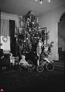 Children with tricycle and wagon next to Christmas tree