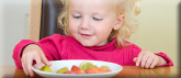 Photo of little girl eating pieces of fruit from a white plate.
