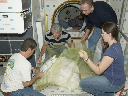 United Space Alliance technicians Troy Mann, Mark Shimei, Jim Smodell and Kelly Gattuso carefully wrap the lower portion of an Extravehicular Mobility Unit (EMU) spacesuit prior to removal from Space Shuttle Endeavour.
