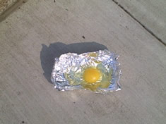 Photo: an egg on tin foil, resting on  cement pavement.