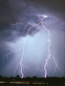 Lightning issuing from  a sky  full of dark clouds strikes the ground.