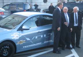 Photo of a small blue car, the Chevy Volt, with GM CEO Rick Wagoner, Senator Carl Levin and Rep. Sander Levin standing alongside the car.