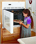 Photo of a little girl taking a pizza out of an oven.