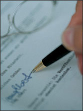 Photo of a person's hand signing a contract or letter.