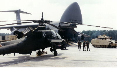 Tank getting ready to be loaded onto a C5 plane and an Apache helicopter 
  alongside on the runway at Hunter Army Airfield