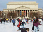 Photo of people ice skating on the Sculpture Garden rink with the Archives building in the background. 