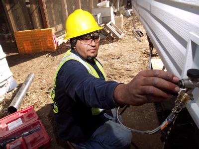 Delzura, CA, December 5, 2007 -- Jaime Castro, of J & J Plumbing, Inc. installs a water facet outside the mobile home a family will temporarily li...