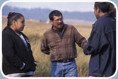 A Native American youth worker stands outside with a Native American boy and girl.