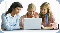 Three women work together on a laptop computer.