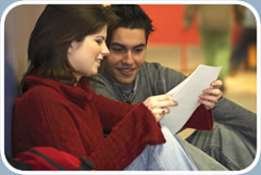 A teenage boy and girl review an assignment while sitting on the floor of a school hallway.