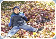 A young boy plays outside in a pile of leaves in the fall.