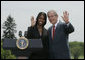 President George W. Bush and Kim Oliver, the 2006 National Teacher of the Year, wave from the podium on the South Lawn Wednesday, April 26, 2006, during a ceremony honoring the Silver Spring, Maryland kindergarten teacher.  White House photo by Paul Morse