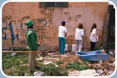 An adult supervises three youths painting over graffiti on an exterior wall.