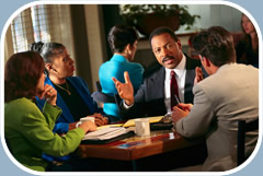 Two men and two women are conversing while seated at a table. They are dressed in business attire.