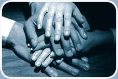 Business professionals stack their outreached hands on top of one another in the center of a table.