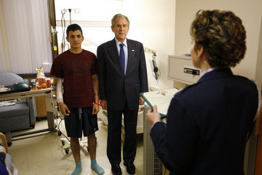 President George W. Bush stands with U.S. Army Specialist Fernando Aguilar of Tucson, Ariz., Monday, Dec. 22, 2008 at Walter Reed Army Medical Center in Washington, D.C., as a White House military aide reads Aguilar's Purple Heart citation. Aguilar is recovering from injuries sustained when two hand grenades were thrown at his vehicle while on patrol in support of Operation Iraqi Freedom. White House photo by Eric Draper